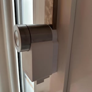 Könnte beinhalten: Nahaufnahme eines silbernen und weißen Türschlosses mit einem runden Knauf. Das Schloss ist an einem weißen Türrahmen montiert.