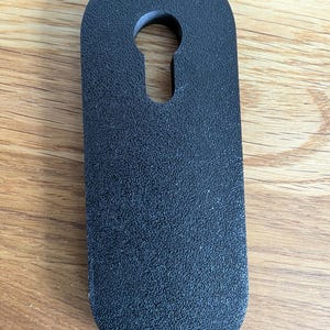 Op de afbeelding: Zwarte plastic deurstop met een sleutelgat uitsnijding. De deurstop heeft een gestructureerd oppervlak.