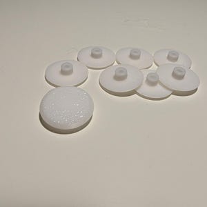 以下が含まれることがあります： 表面がテクスチャ加工された白いプラスチック製の家具の足が8つ。足には小さな隆起した中心があります。
