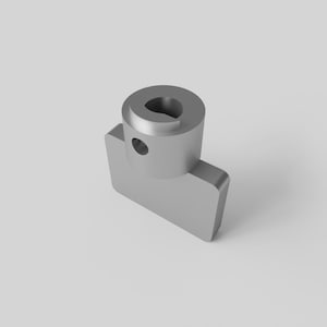 Può includere: Un componente meccanico color argento con una parte superiore cilindrica e una base rettangolare. La parte superiore presenta un'apertura a forma di buco della serratura e un piccolo foro circolare sul lato. La base ha bordi arrotondati.