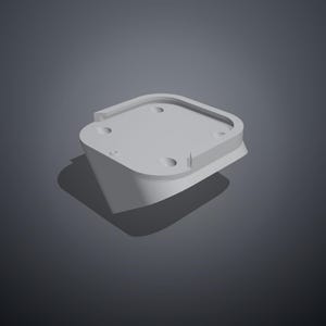 May include: A light grey, square-shaped mounting bracket with rounded corners. The top surface features a raised perimeter edge and four circular screw holes positioned near each corner. The component has a solid, angled base structure.