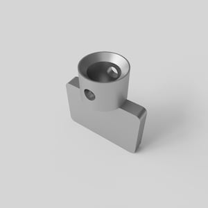 Op de afbeelding: Een zilverkleurig, geometrisch object met een cilindrische bovenkant en een rechthoekige basis. De cilindrische bovenkant heeft een cirkelvormige opening en een kleiner gat aan de zijkant. De basis is rechthoekig met afgeronde randen.