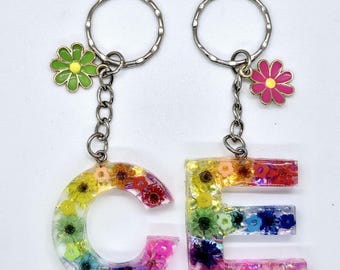 May include: Two keychains with the letters C and E made of clear resin with colorful pressed flowers inside. Each keychain has a small metal flower charm, one green and one pink.