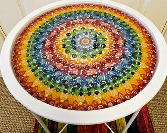 Puede incluir: Mesa redonda blanca con un diseño de mosaico colorido hecho de pequeños trozos de papel redondos. El diseño del mosaico es un mandala arcoíris con un círculo central.