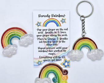 May include: A rainbow-colored keychain with a card that reads "Remedy Rainbow" and instructions on how to use the keychain for stress relief. The card says "Pop your finger on the red arch, breathe in & trace your finger along the arch. Move to Orange & breathe out tracing back to the other side. Repeat process until your rainbow has worked its magic. Everything will be OK. You've got this!"
