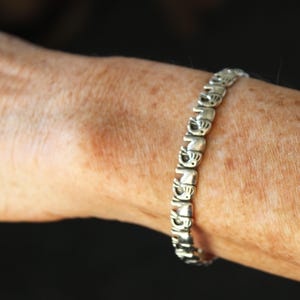 Puede incluir: Un brazalete de plata con un patrón repetido de pequeñas figuras de elefantes.