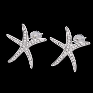 May include: A pair of silver-toned starfish stud earrings featuring a metallic finish and embedded with numerous small, clear, sparkling stones along the surface of each arm, complete with clear plastic earring backs for secure attachment.