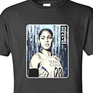 May include: Black t-shirt featuring a portrait of a basketball player. The portrait is in a rectangular frame and includes the text "MAYA MOORE 123" and "23 MOORE". The shirt also has a QR code.