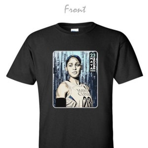 May include: Black t-shirt featuring a graphic of a woman in a basketball jersey. The jersey has the text "Mayo Clinic" and the number "23". The image also includes the name "Moore" and the number "23".