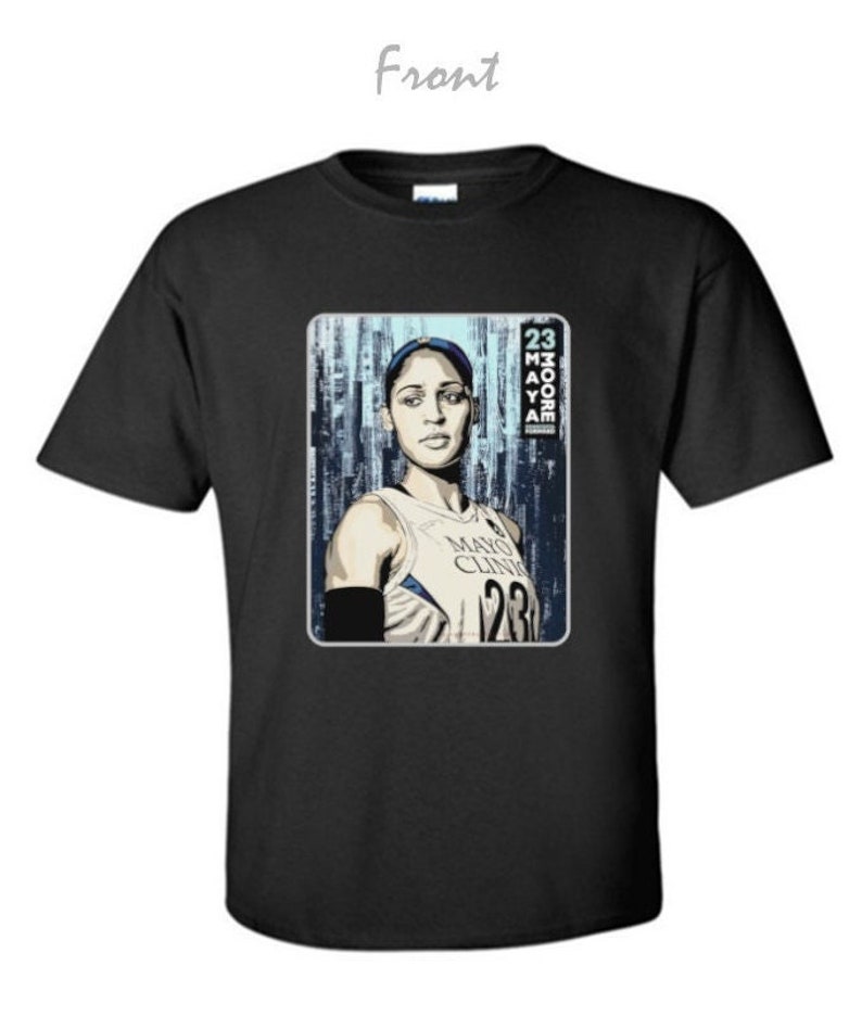May include: Black t-shirt featuring a graphic of a woman in a basketball jersey. The jersey has the text "Mayo Clinic" and the number "23". The image also includes the name "Moore" and the number "23".