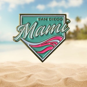 May include: A gold-colored baseball-shaped pin with a teal blue background and white and pink waves. The text "SAN DIEGO" and "Mami" are printed on the pin.