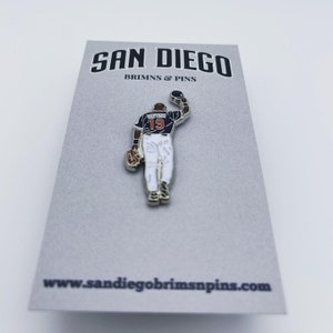 May include: A silver baseball player pin with a black and white uniform, orange number 19, and a black baseball. The pin is on a gray card with the text "SAN DIEGO BRIMS & PINS" and "www.sandiegobrimspins.com".