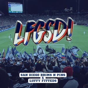 May include: A metal pin with the text "LFCSD!" in white, blue, and orange, with a silver outline. The pin is set against a backdrop of a soccer stadium filled with fans and flags. The text "SAN DIEGO BRIMS N PINS & LUFFY FITTEDS" is at the bottom.