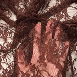 Puede incluir: Una tela de encaje de color marrón oscuro transparente que presenta un intrincado patrón floral. El material es ligero y semitransparente, con una delicada construcción de malla que permite la visibilidad a través del diseño calado.