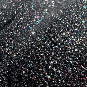 Pode incluir: Tecido preto com uma superf&iacute;cie texturizada coberta de glitter iridescente. O glitter &eacute; uma mistura de cores prata, ouro e arco-&iacute;ris.