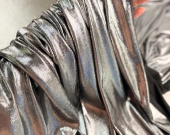 May include: Close-up of a silver metallic fabric with a crinkled texture. The fabric is soft and flowing, with a subtle sheen.