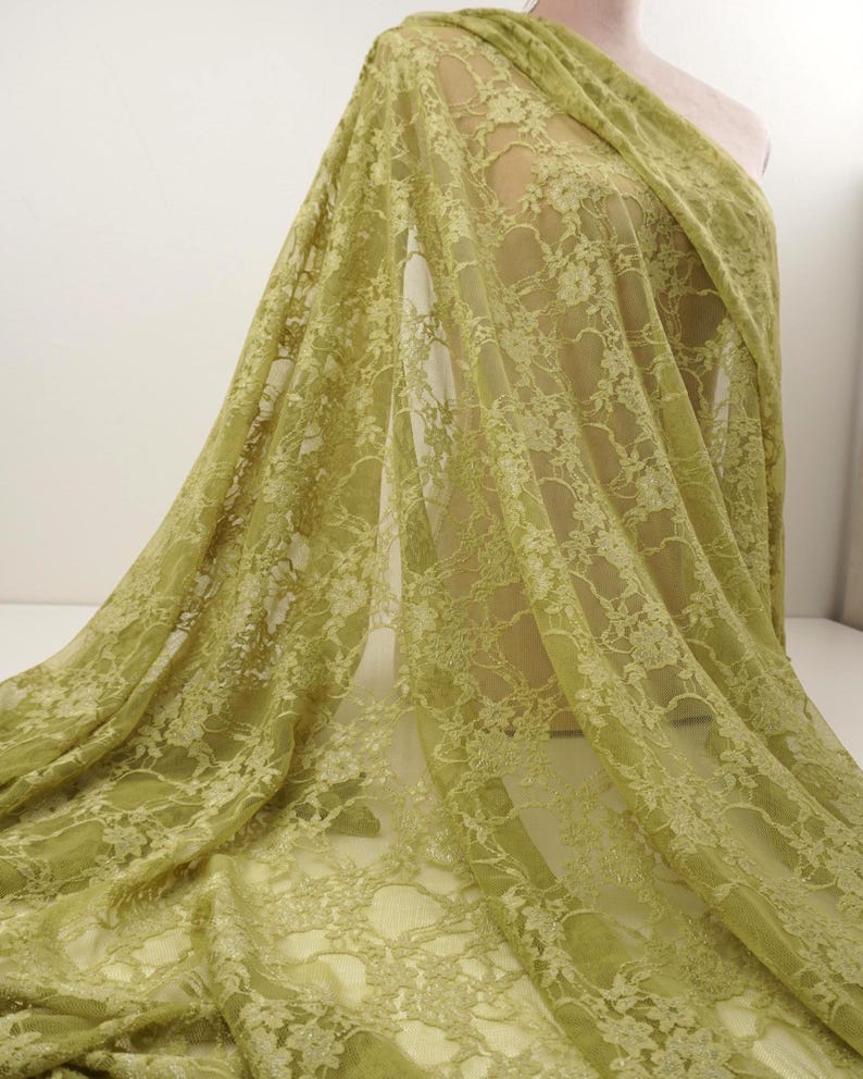 May include: A draped length of olive green lace fabric. The delicate floral pattern is visible throughout the sheer material. The fabric is draped over a mannequin, showcasing its flow and texture. Ideal for apparel or craft projects.