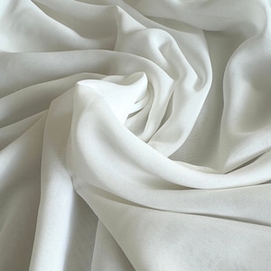 以下が含まれることがあります： 柔らかな折り目とシワのある白い透き通った生地。生地は滑らかで繊細で、かすかな光沢があります。