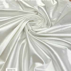 K&ouml;nnte beinhalten: Wei&szlig;er Braut-Satin, dick und gl&auml;nzend. Der Stoff ist gefaltet und drapiert und zeigt seine Textur und seinen Fall.
