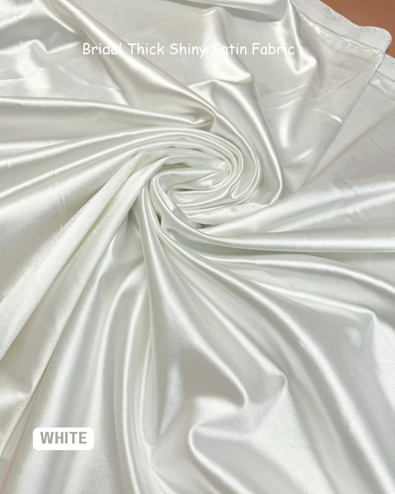 K&ouml;nnte beinhalten: Wei&szlig;er Braut-Satin, dick und gl&auml;nzend. Der Stoff ist gefaltet und drapiert und zeigt seine Textur und seinen Fall.