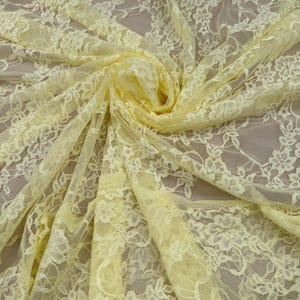 Close Up Detail Of Yellow Floral Stretch Lace Fabric Against A Hand To Show The Intricate Rose Pattern And Sheer 4-Way Stretch Texture For Designers.