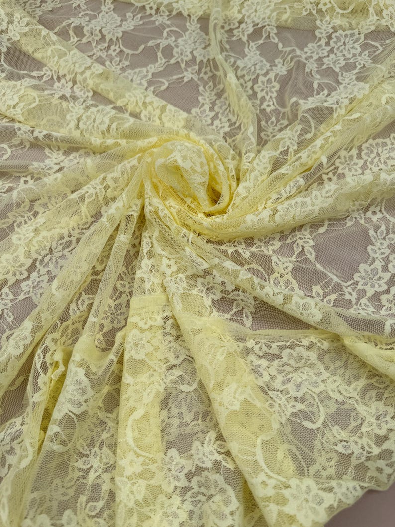 Close Up Detail Of Yellow Floral Stretch Lace Fabric Against A Hand To Show The Intricate Rose Pattern And Sheer 4-Way Stretch Texture For Designers.