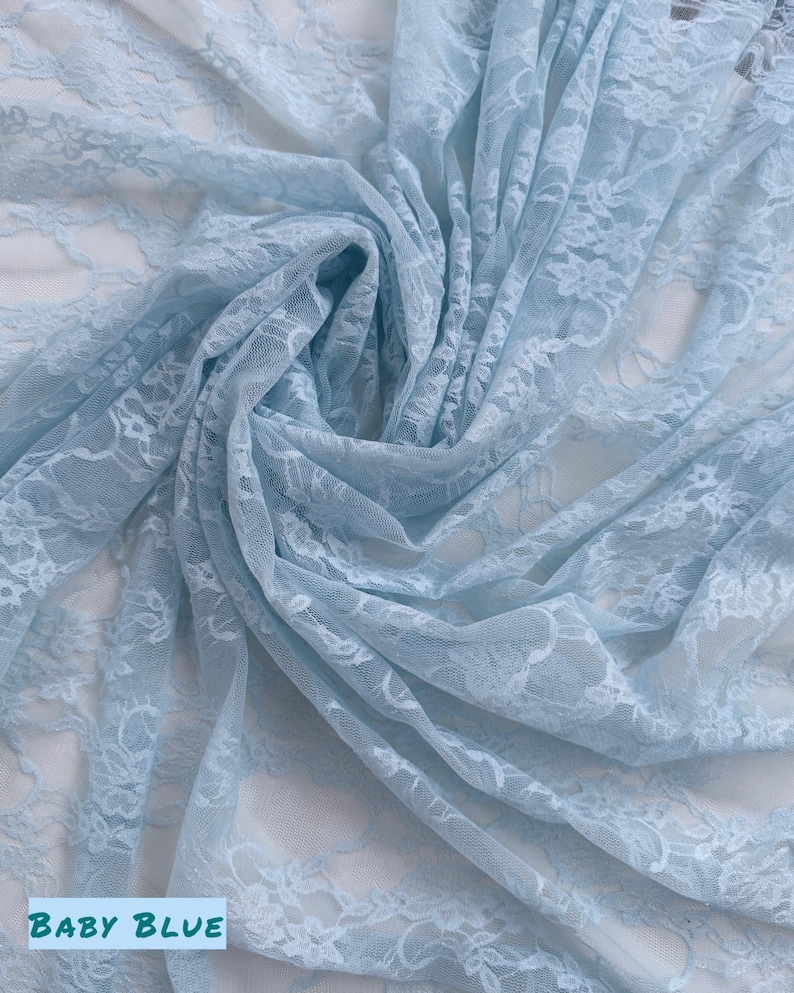 May include: Baby blue lace fabric with a floral pattern, draped and folded. The fabric is a light, airy material, with the words "BABY BLUE" in a white box at the bottom.