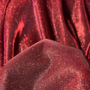 May include: Close-up of a red fabric with a sparkly, glittery texture. The fabric is folded and draped, creating a soft, flowing look.