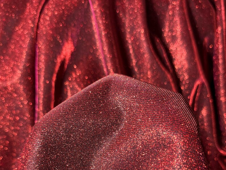 May include: Close-up of a red fabric with a sparkly, glittery texture. The fabric is folded and draped, creating a soft, flowing look.