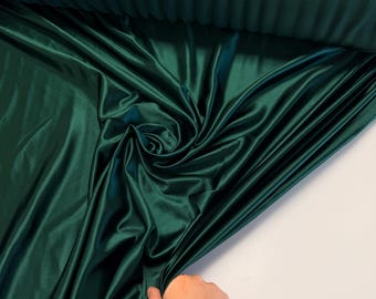Könnte beinhalten: Ein tiefgrüner Satin-Stoff mit einer glatten, seidenartigen Textur. Der Stoff ist gefaltet und drapiert und zeigt seinen luxuriösen Glanz.