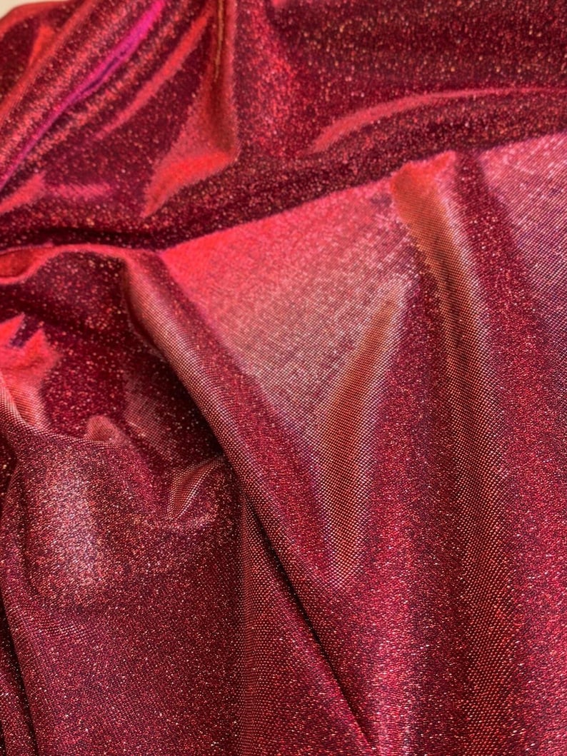 May include: Close-up of a red fabric with a sparkly, iridescent finish. The fabric has a subtle texture and a slight sheen.