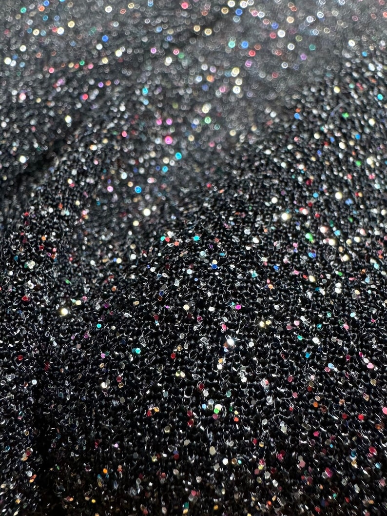 Pode incluir: Tecido preto com uma superf&iacute;cie texturizada coberta de glitter iridescente. O glitter &eacute; uma mistura de cores prata, ouro e arco-&iacute;ris.