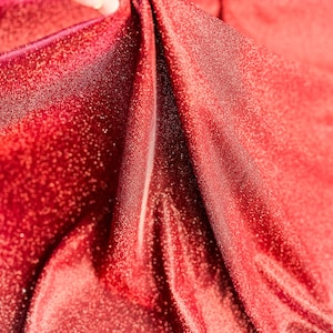 May include: Close-up of red fabric with a sparkly texture. The fabric is folded and draped, creating a soft, flowing look.