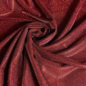 May include: Red sparkly fabric with a shimmery finish. The fabric is folded and draped, showing its texture and sheen.
