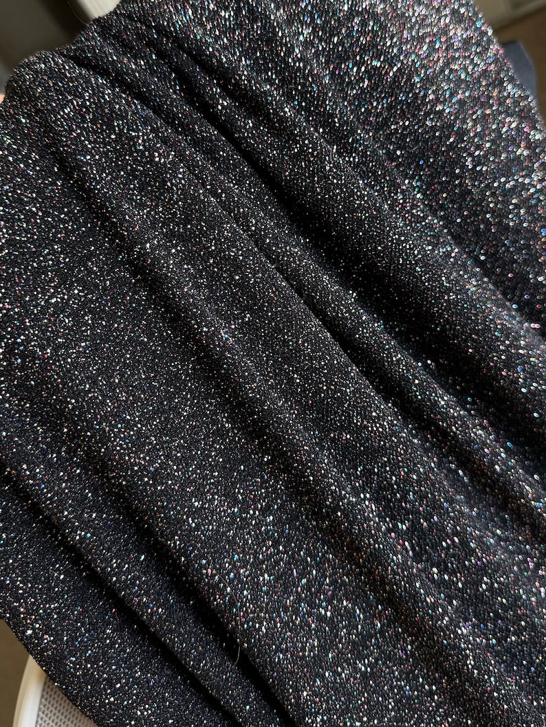 Pode incluir: Close-up de tecido preto com glitter iridescente. O tecido tem uma apar&ecirc;ncia texturizada e tecida.