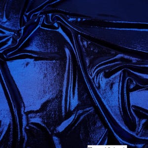 May include: A piece of fabric with a metallic royal blue finish on the top surface and a solid black underside. The material is draped to show folds and light reflections. A white rectangular label with the text Royal/black is visible.