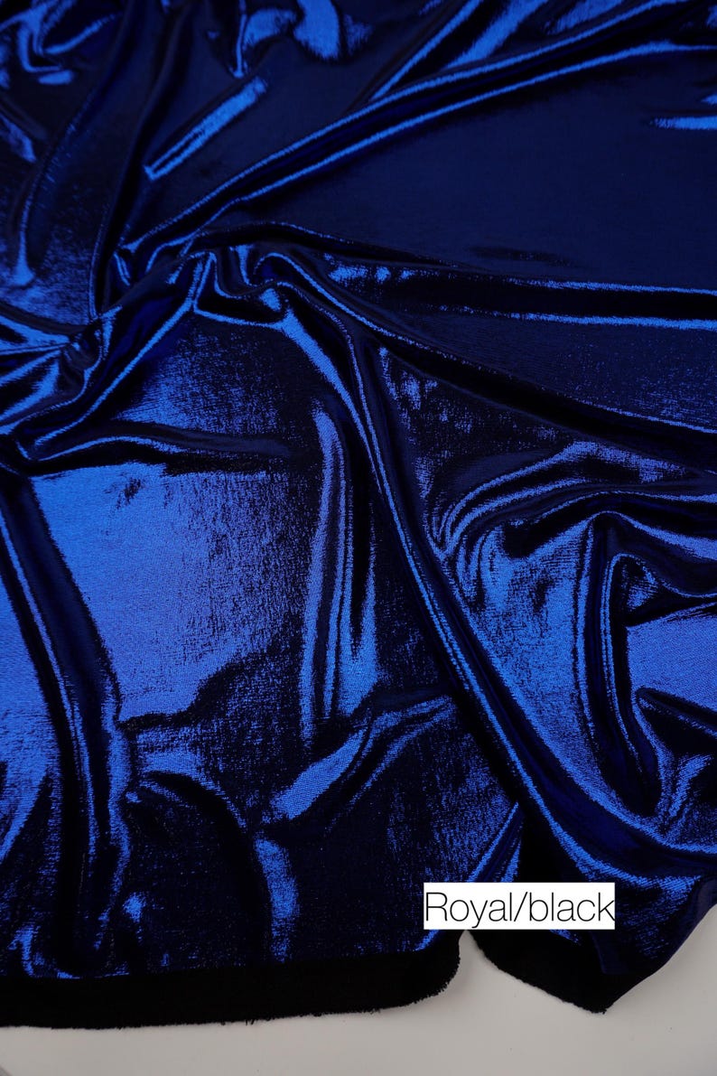 May include: A piece of fabric with a metallic royal blue finish on the top surface and a solid black underside. The material is draped to show folds and light reflections. A white rectangular label with the text Royal/black is visible.