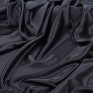 May include: A length of dark charcoal gray fabric with a smooth, lustrous finish. The material is draped in deep, flowing folds that create a series of highlights and shadows across the surface, emphasizing the soft texture of the textile.