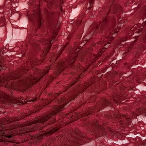 K&ouml;nnte beinhalten: Nahaufnahme eines tiefroten Spitzenstoffs. Das zarte Blumenmuster ist im gesamten Material sichtbar. Der Stoff ist drapiert, wodurch Schatten entstehen und die Textur hervorgehoben wird. Die Spitze wird wahrscheinlich f&uuml;r Kleidung oder Bastelprojekte verwendet.