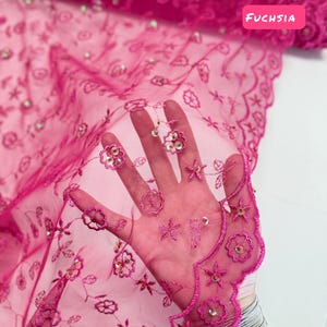 Peut inclure: Tissu en dentelle brod&eacute;e fuchsia avec des motifs floraux et &eacute;toil&eacute;s. Le tissu semi-transparent pr&eacute;sente un bord festonn&eacute; et des paillettes iris&eacute;es. Les textes "FUCHSIA" et "LIMITED STOCK Will Not Be Restocked" sont visibles.