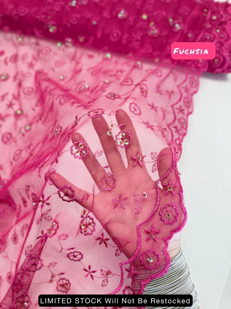 Peut inclure: Tissu en dentelle brod&eacute;e fuchsia avec des motifs floraux et &eacute;toil&eacute;s. Le tissu semi-transparent pr&eacute;sente un bord festonn&eacute; et des paillettes iris&eacute;es. Les textes "FUCHSIA" et "LIMITED STOCK Will Not Be Restocked" sont visibles.