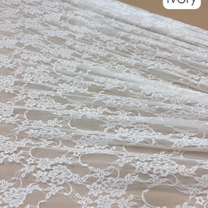 May include: Ivory-colored lace fabric, 58/60 inches wide, with a delicate floral pattern. The fabric is draped, showing the intricate design and texture. The word "Ivory" is displayed in a white box.