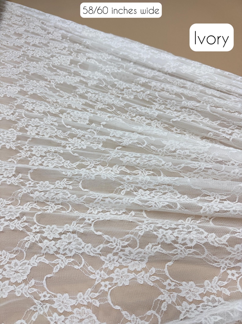May include: Ivory-colored lace fabric, 58/60 inches wide, with a delicate floral pattern. The fabric is draped, showing the intricate design and texture. The word "Ivory" is displayed in a white box.
