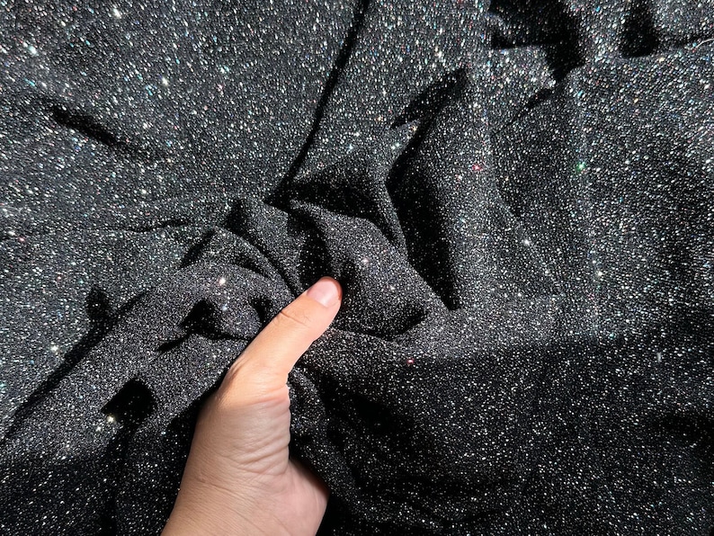 Pode incluir: Close-up de um tecido preto com um acabamento brilhante e iridescente. O tecido est&aacute; enrugado e tem uma superf&iacute;cie texturizada.