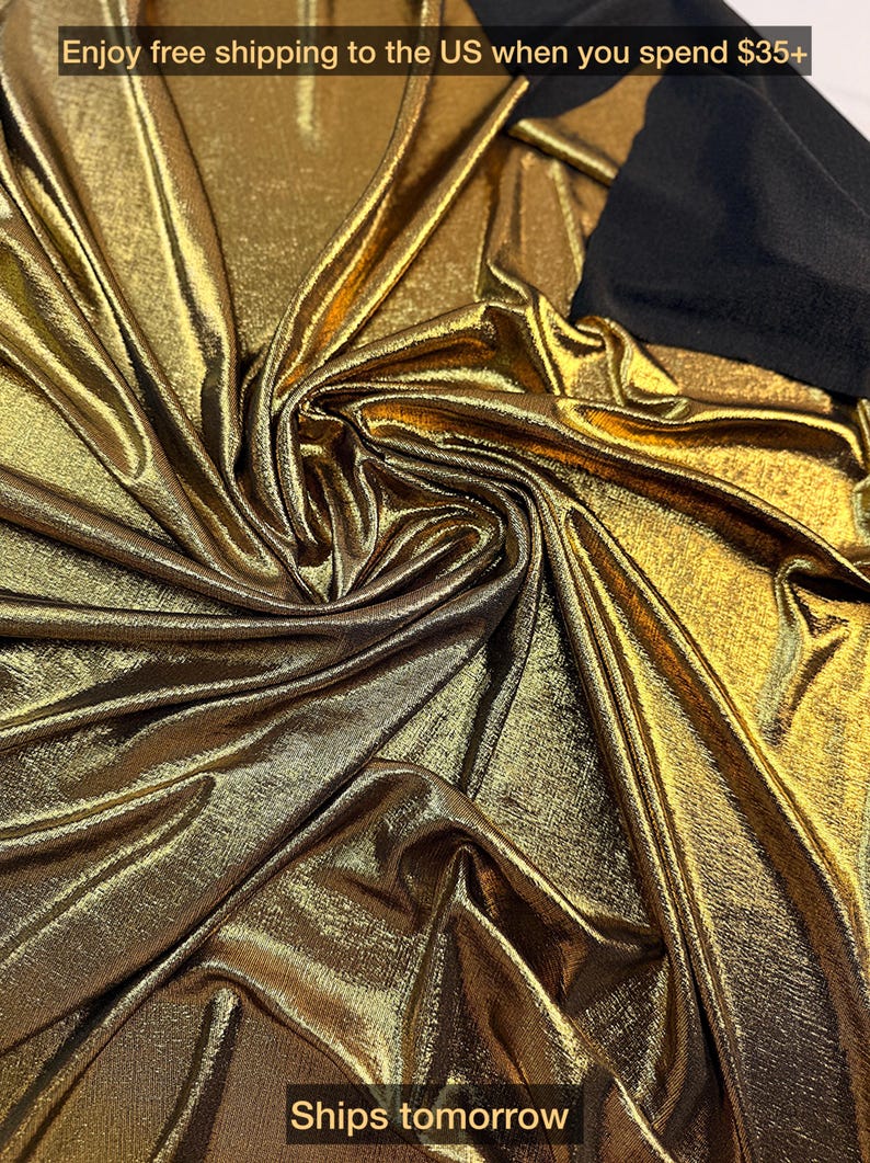 May include: A metallic gold fabric with a shimmering, reflective surface and deep, flowing folds. The material features a dense, textured weave that catches the light, contrasted by a solid black fabric section visible at the top right corner.