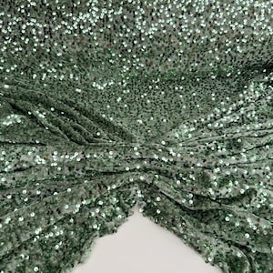 Op de afbeelding: Groene paillettenstof met een zachte, glinsterende textuur. De pailletten zijn klein en gelijkmatig verdeeld, waardoor een subtiel glinsterend effect ontstaat.