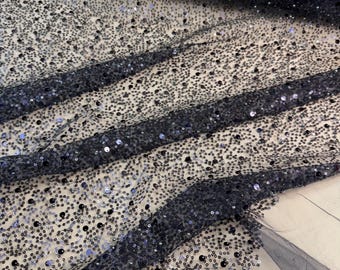 Könnte beinhalten: Nahaufnahme eines marineblauen Stoffes, der mit kleinen, schimmernden Pailletten bedeckt ist. Der Stoff ist drapiert und erzeugt Falten und Schatten, die die Textur und den Glanz der Pailletten hervorheben. Der Gesamteffekt ist luxuriös und elegant.