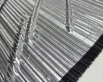 May include: Silver pleated fabric with a black ruffled trim. The fabric has a metallic sheen and a textured, crinkled look.