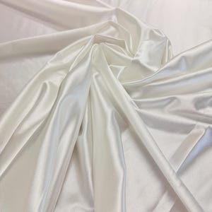 K&ouml;nnte beinhalten: Wei&szlig;er Satin-Stoff mit einer glatten, seidenartigen Textur. Der Stoff ist drapiert und gefaltet und zeigt seine luxuri&ouml;se Haptik.