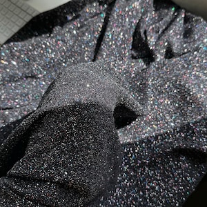 Pode incluir: Tecido preto com glitter iridescente. O tecido &eacute; texturizado e tem um brilho sutil.